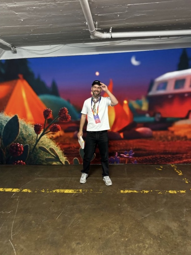 An attendee smiling in front of the campfire mural