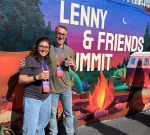 Two attendees smiling together beside the Summit mural